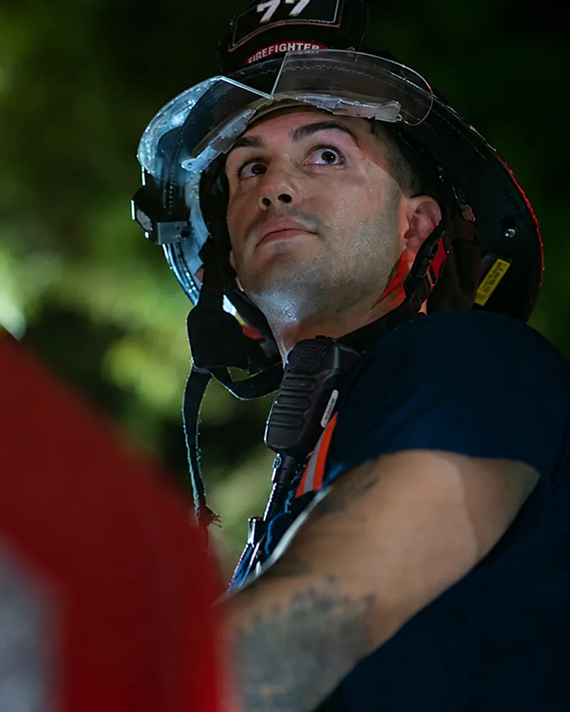 Firefighter in turnout gear and helmet listening to a portable radio on scene